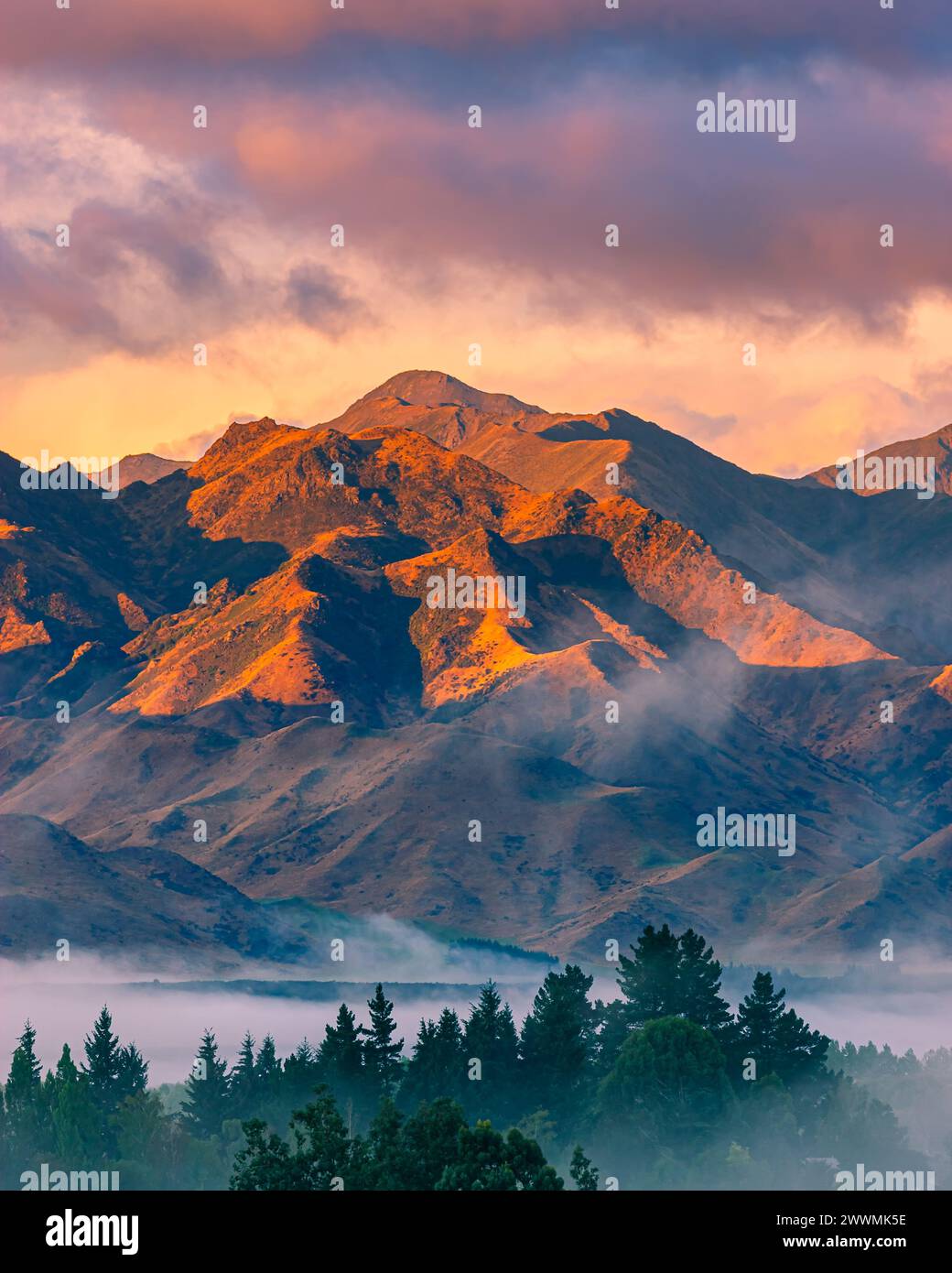 A vertical 4:5 photo of a sunrise with colorful clouds over the mountains and morning mist in the valley in Hanmer Springs, a town in the Canterbury r Stock Photo