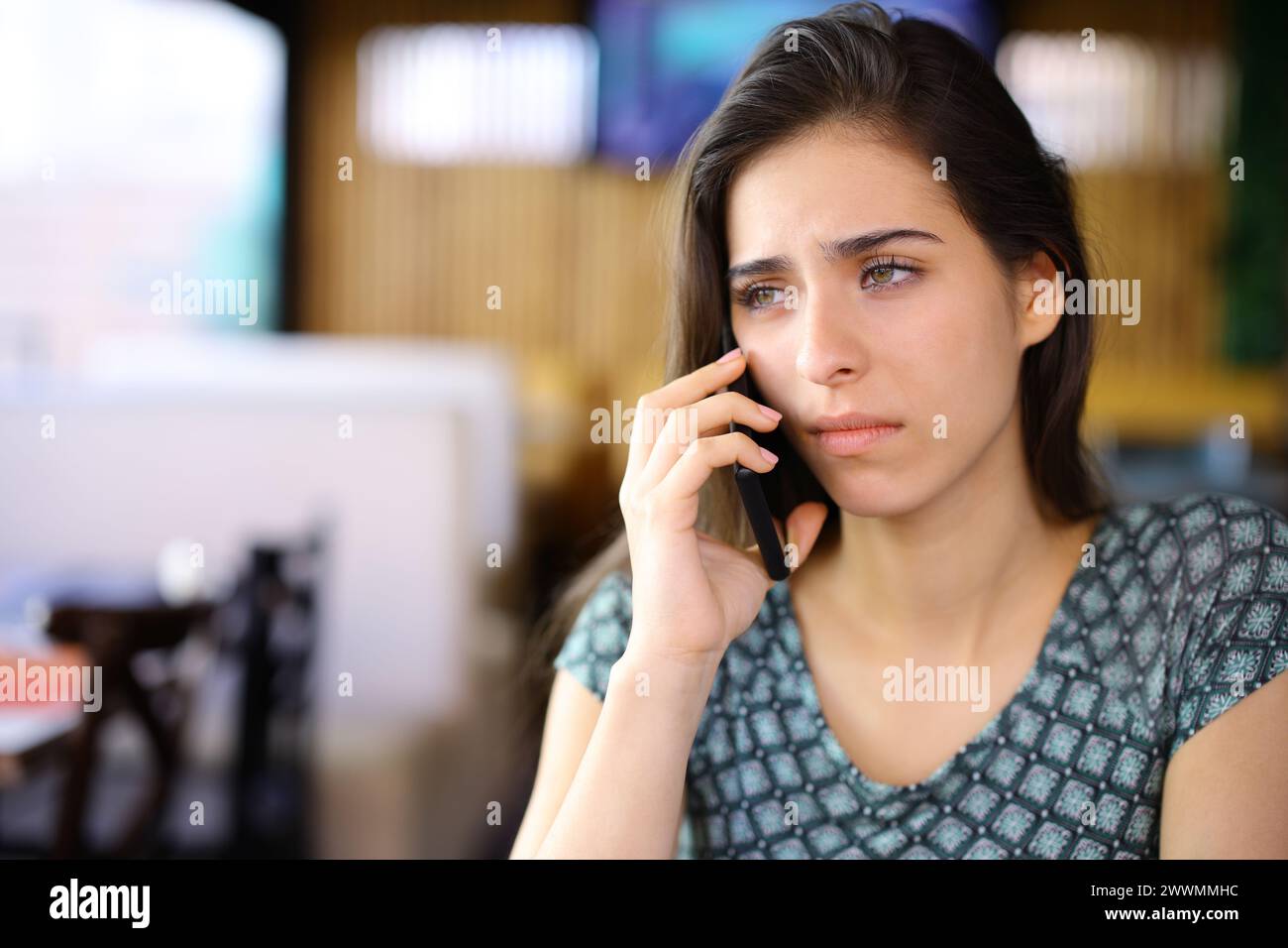 Sad woman talking on phone in a bar interior Stock Photo