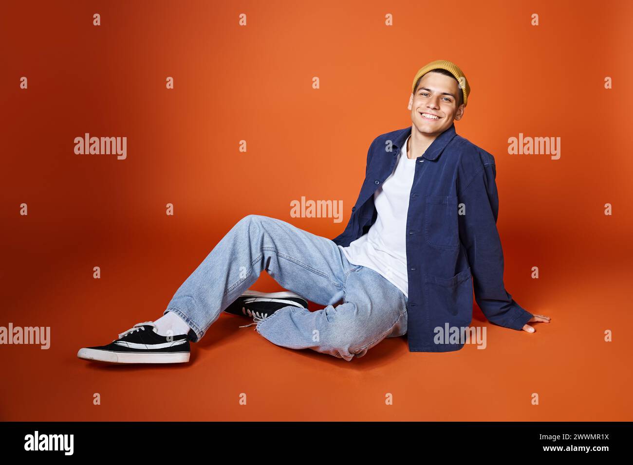smiling man in his 20s relaxed sitting leaning on hands with backpack against terracotta background Stock Photo