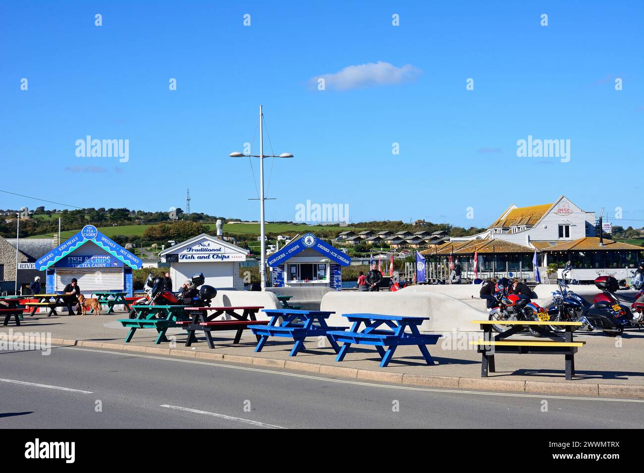 Bikers relaxing on the roadside with The Rise restaurant to the rear and snack kiosks to the left, West Bay, Dorset, UK, Europe. Stock Photo