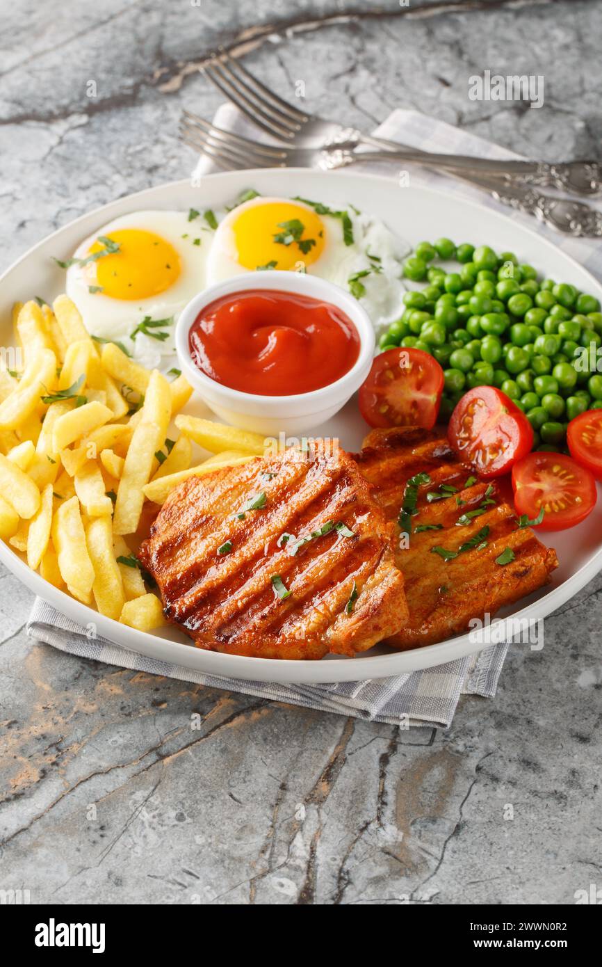 Set lunch Grilled steak with green peas, fried egg, french fries, tomatoes and sauce close-up in a plate on the table. Vertical Stock Photo