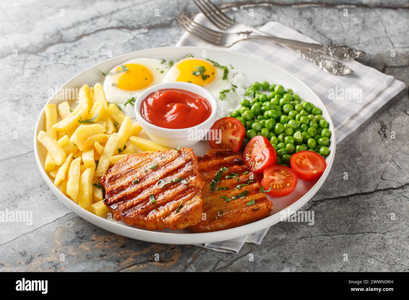 Portion of grilled loin steak with green peas, fried eggs, french fries, fresh tomatoes and sauce close-up in a plate on the table. Horizontal Stock Photo