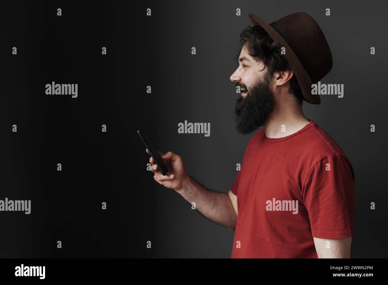Stylish man in hat using smartphone on moody background Stock Photo