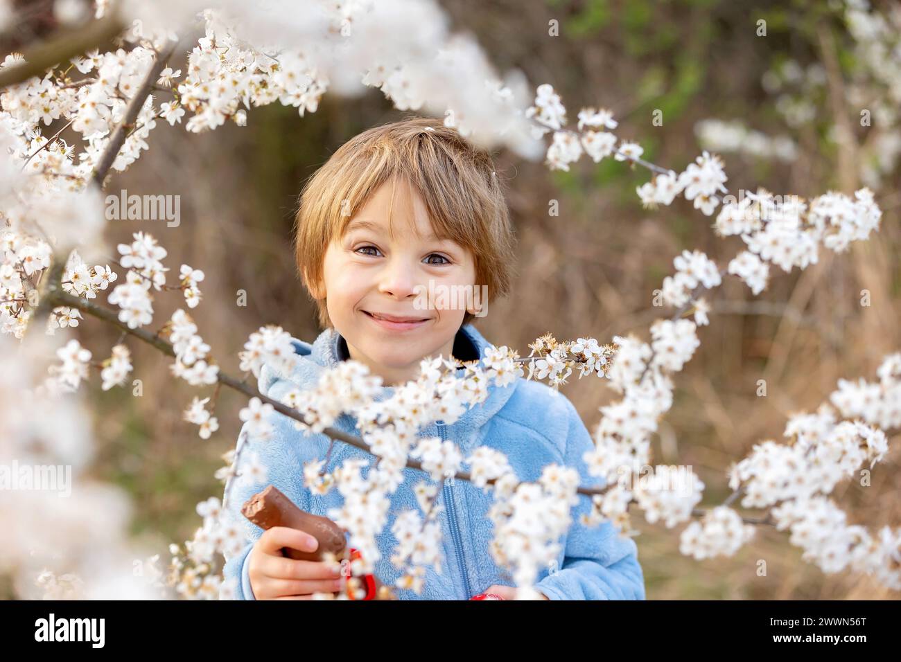 Beautiful blond child, boy, holding twig, braided whip made from pussy willow, traditional symbol of Czech Easter used for whipping girls and basket w Stock Photo