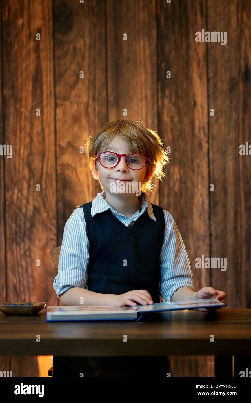 Cute child, boy wearing glasses, reading a book at home, studio shot Stock Photo