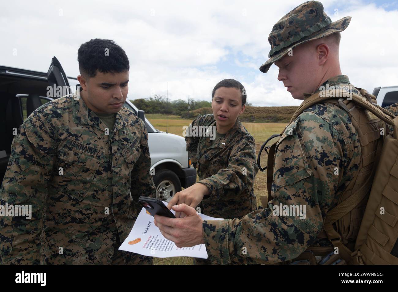 U.S. Marine Corps 1st Lt. Isis Coty, center, and Cpl. Hernandez, left, with Marine Aircraft Group (MAG) 24, 1st Marine Aircraft Wing, show a menu to a Marine on the rifle range during a volunteer event at Puuloa Range Training Facility, Ewa beach, Feb. 22, 2024. Marines with MAG-24 prepared and sold burgers, hotdogs, chips and drinks to Marines on the rifle range to raise funds for the 249th Marine Corps Ball.  Marine Corps Stock Photo