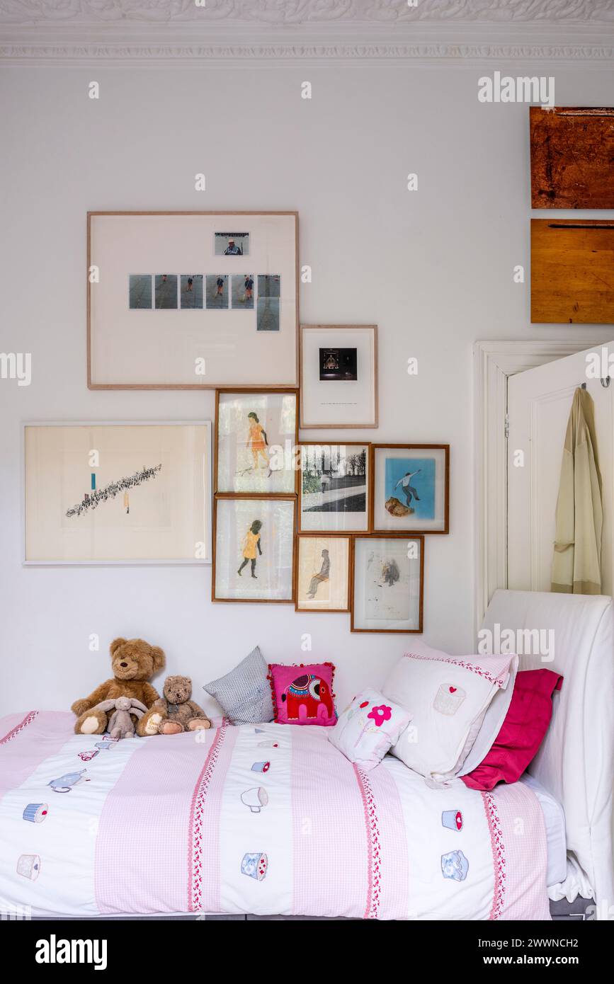 Collection of framed artwork above girl's bed in modern West London