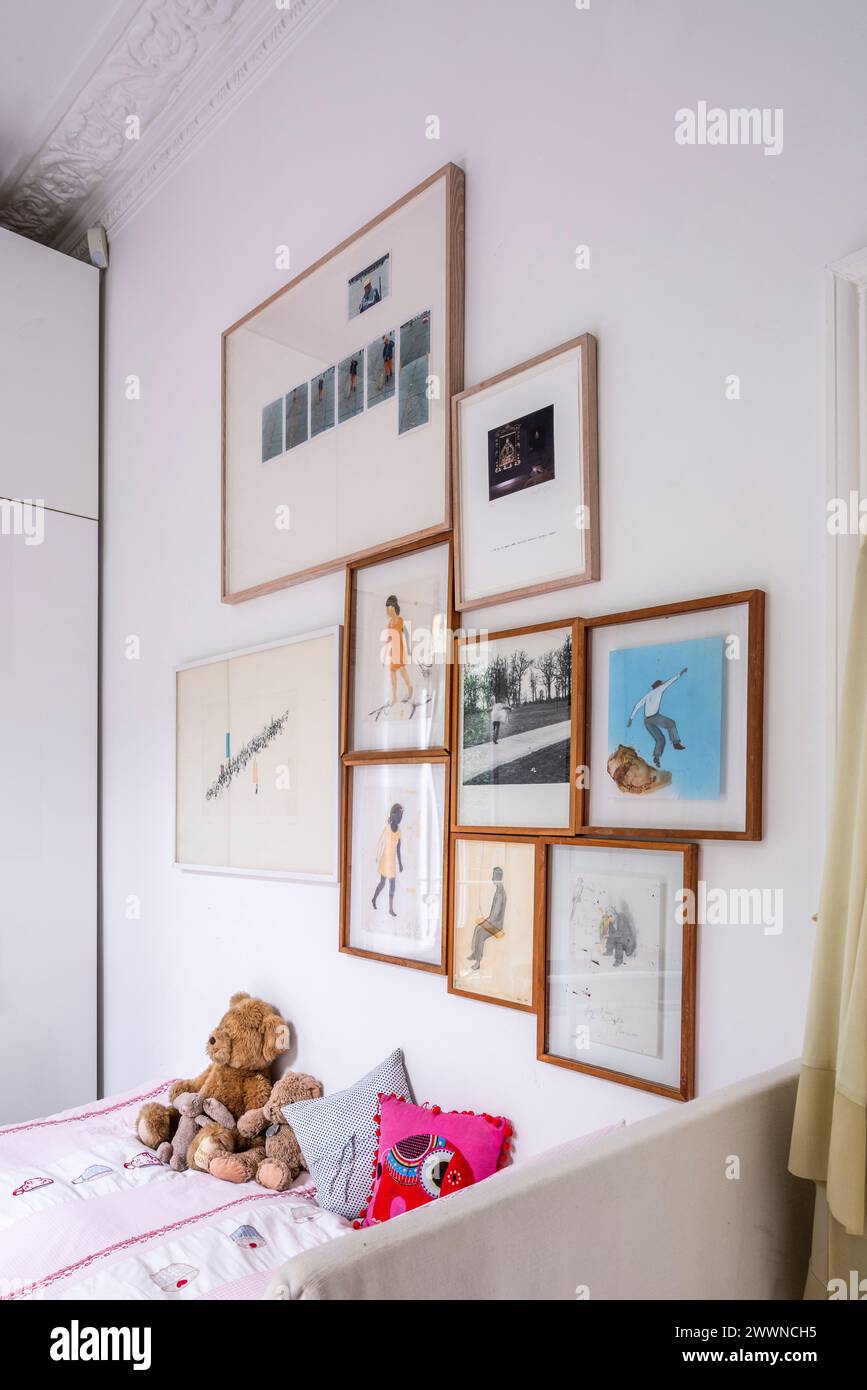 Collection of framed artwork above girl's bed in modern West London