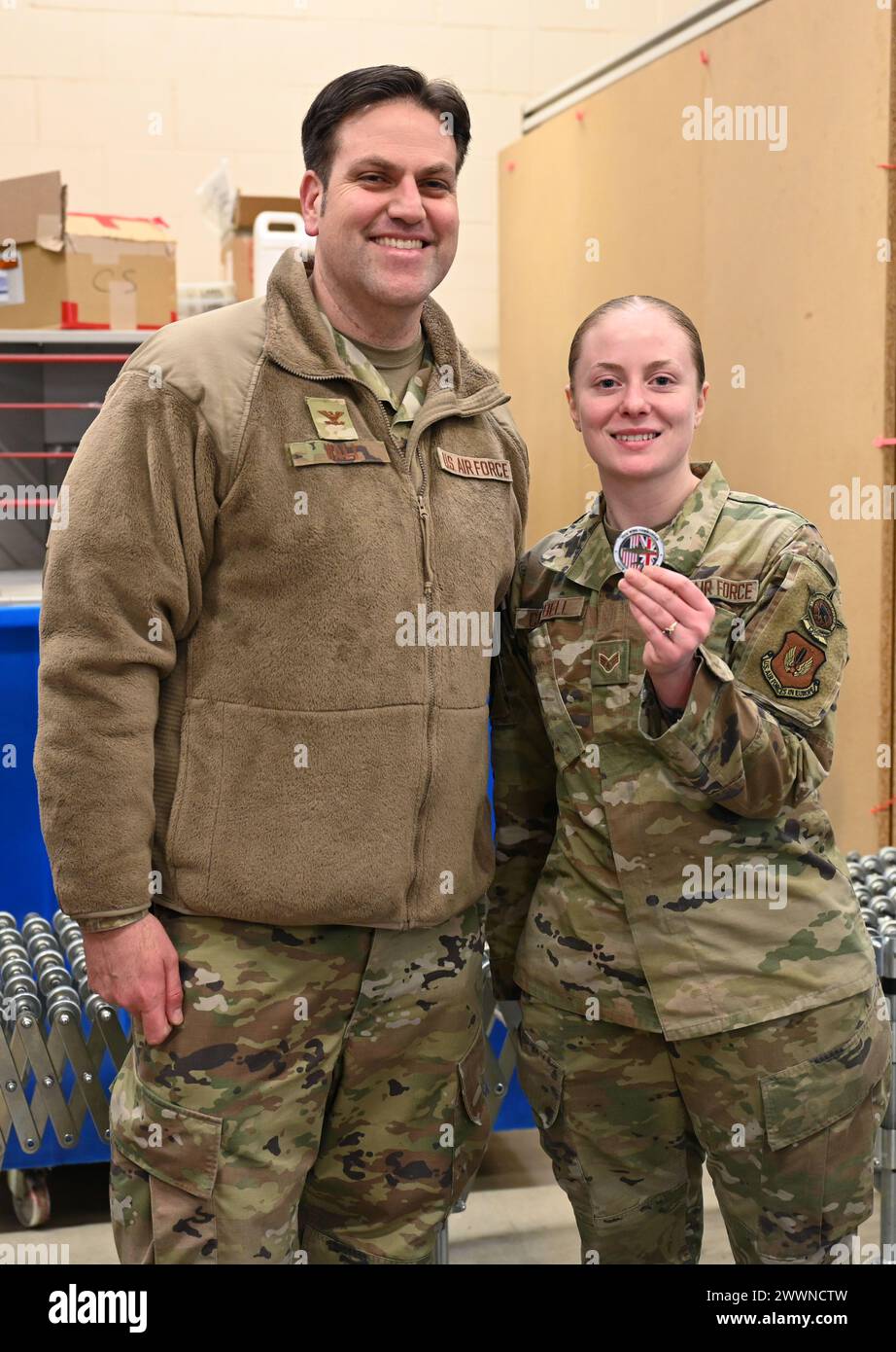 U.S. Air Force Senior Airman Zoie Campbell, right, 100th Force Support Squadron Post Office military postal clerk, shows off her coin presented by Col. Joseph Wall, 100th Air Refueling Wing deputy commander, at Royal Air Force Mildenhall, England, Feb. 2, 2024. Campbell is a section lead and oversees eight Airmen. She leads the postal services center, which includes creating schedules, managing the truck process for parcels received from RAF Alconbury, manages the distribution for RAF Mildenhall, oversees the smart locker program, and is responsible for the security of mail dispatch.  Air Forc Stock Photo