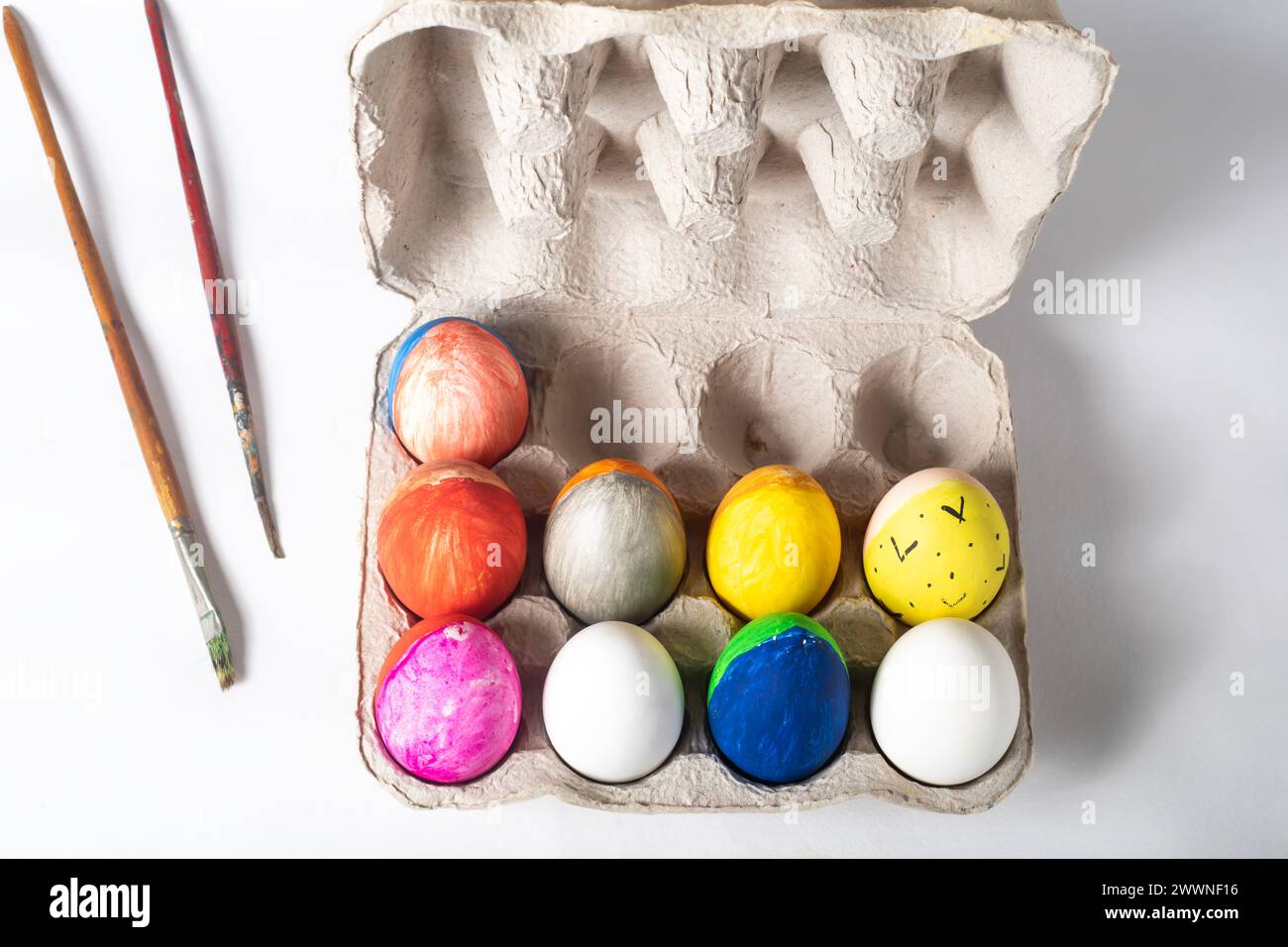 Easter eggs in a cardboard box and paint brushes on a white background, top view Stock Photo
