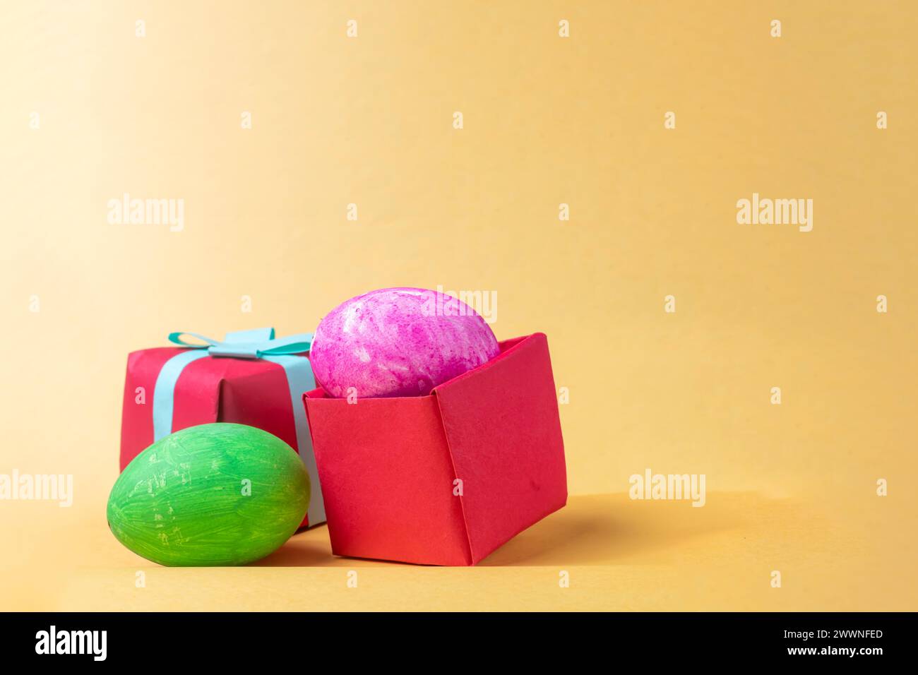 Colorful easter eggs in red gift box on yellow background. Copy space. Stock Photo