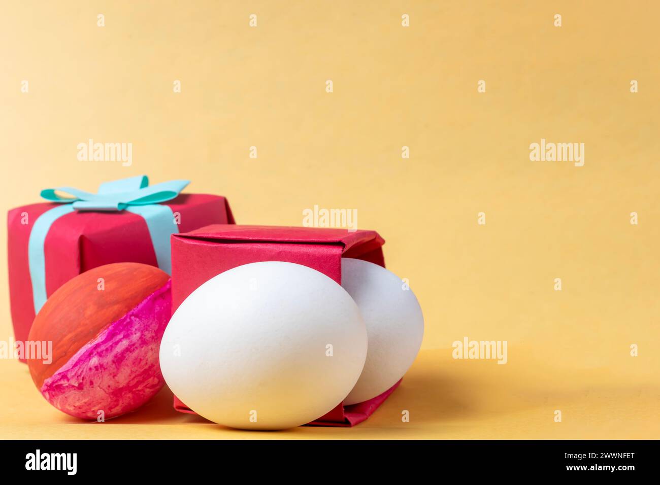 Colorful easter eggs in red gift box on yellow background. Copy space. Stock Photo