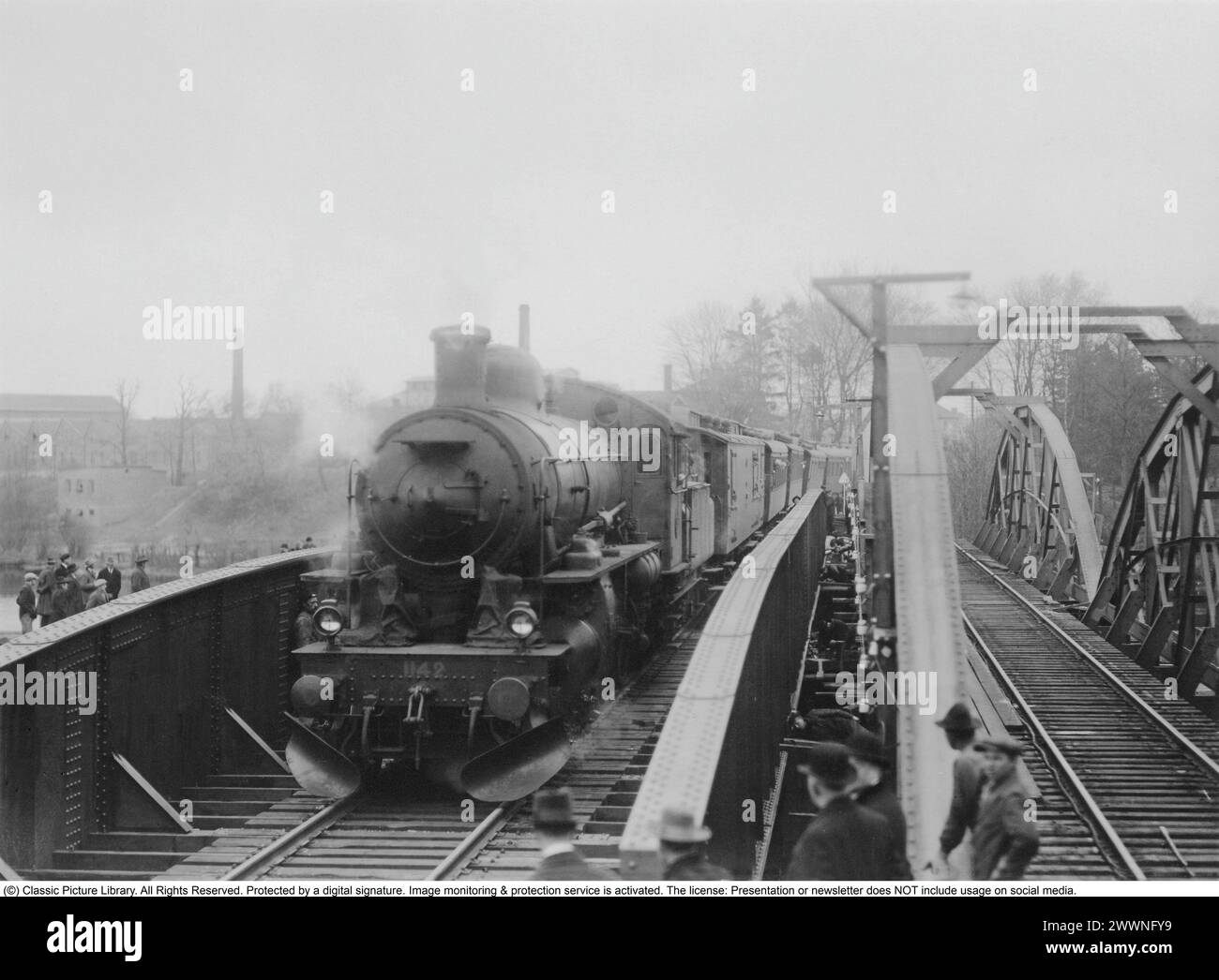 Railway history. The first steam locomotive and wagons cross the new railway bridge over the Nissan waterway at Halmstad. The new steel bridge replaces the old one on the right. People have gathered to watch the first train pass. April 1928 Stock Photo