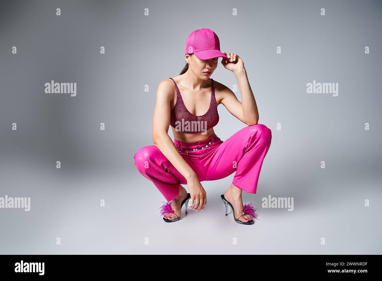 Fancy Brunette Woman In Red Top And Pink Trousers Touching Stylish Cap fancy-brunette-woman-in-red-top-and-pink-trousers-touching-stylish-cap