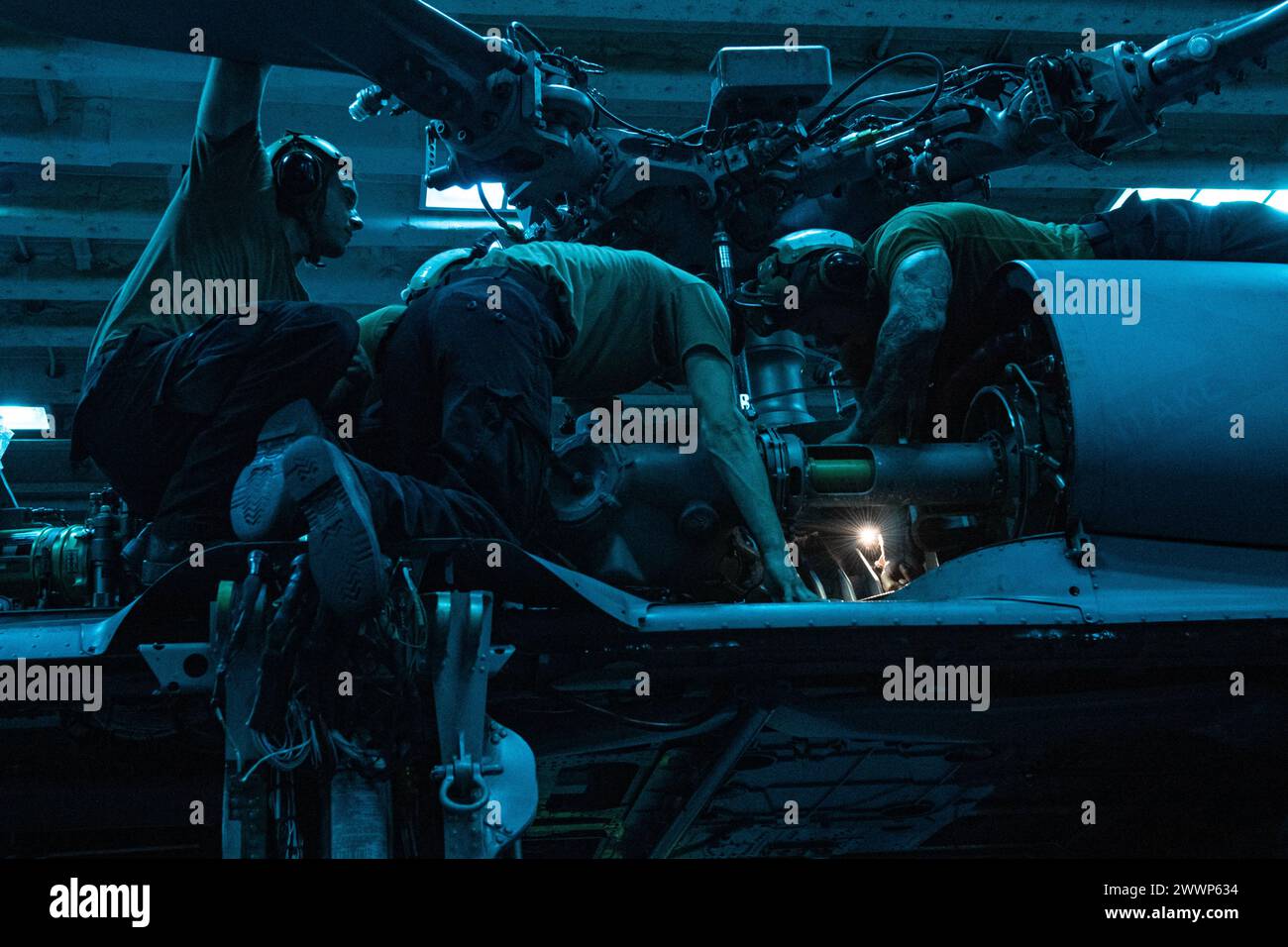 EAST CHINA SEA (February 4, 2024) Sailors assigned to Helicopter Sea Combat Squadron (HSC) 25 perform maintenance on an MH-60S helicopter in the hangar bay of the forward-deployed amphibious assault carrier USS America (LHA 6), while conducting routine operations in the East China Sea, February 4. America, lead ship of the America Amphibious Ready Group, is operating in the U.S. 7th Fleet area of operations. U.S. 7th Fleet is the U.S. Navy’s largest forward-deployed numbered fleet, and routinely interacts and operates with allies and partners in preserving a free and open Indo-Pacific region. Stock Photo