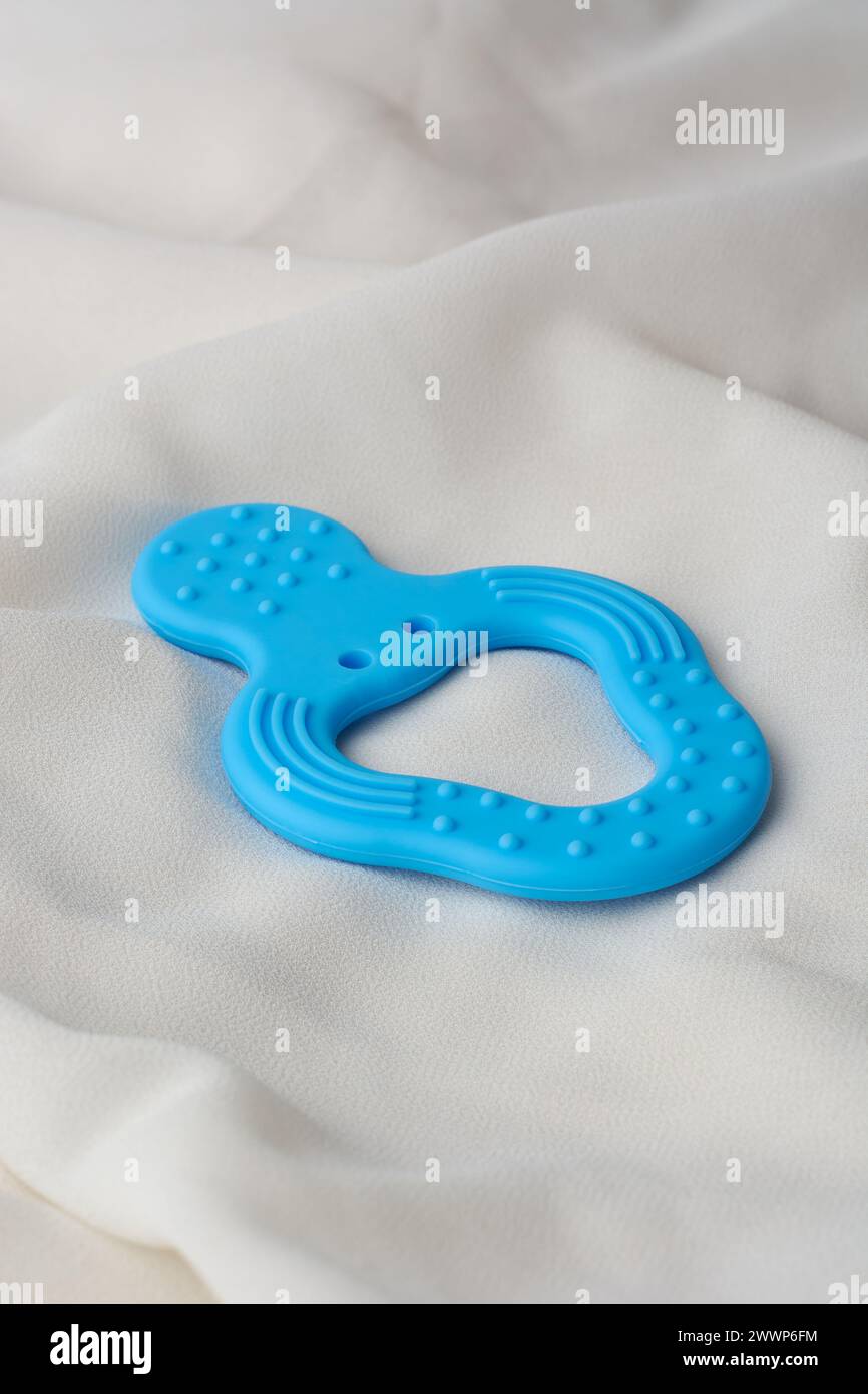 blue color natural rubber baby teether on white textured fabric surface, soothing aids for teething babies to chew on, free from harmful chemicals Stock Photo