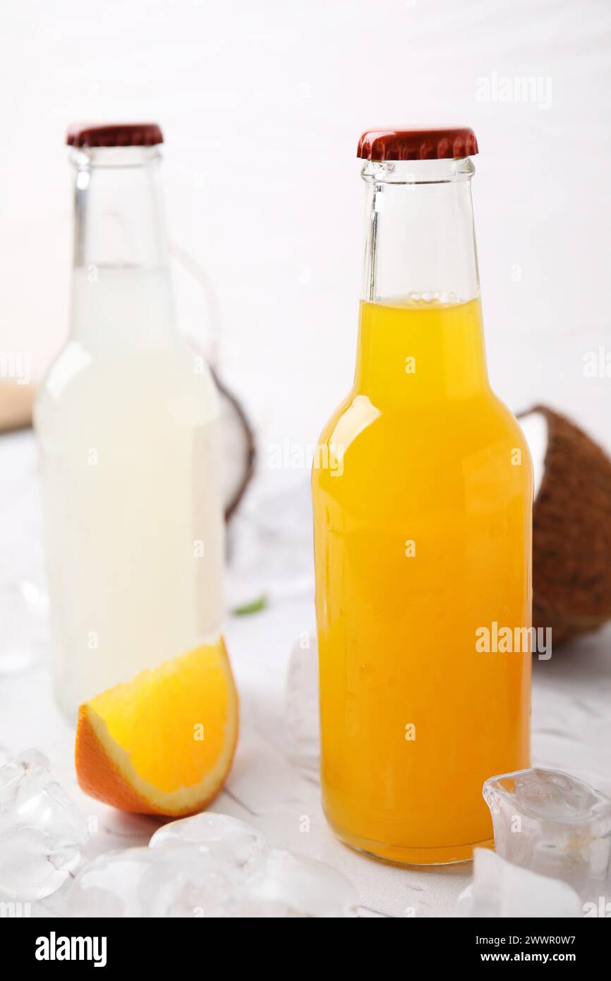 Tasty kombucha in glass bottles, orange and ice on white table Stock Photo