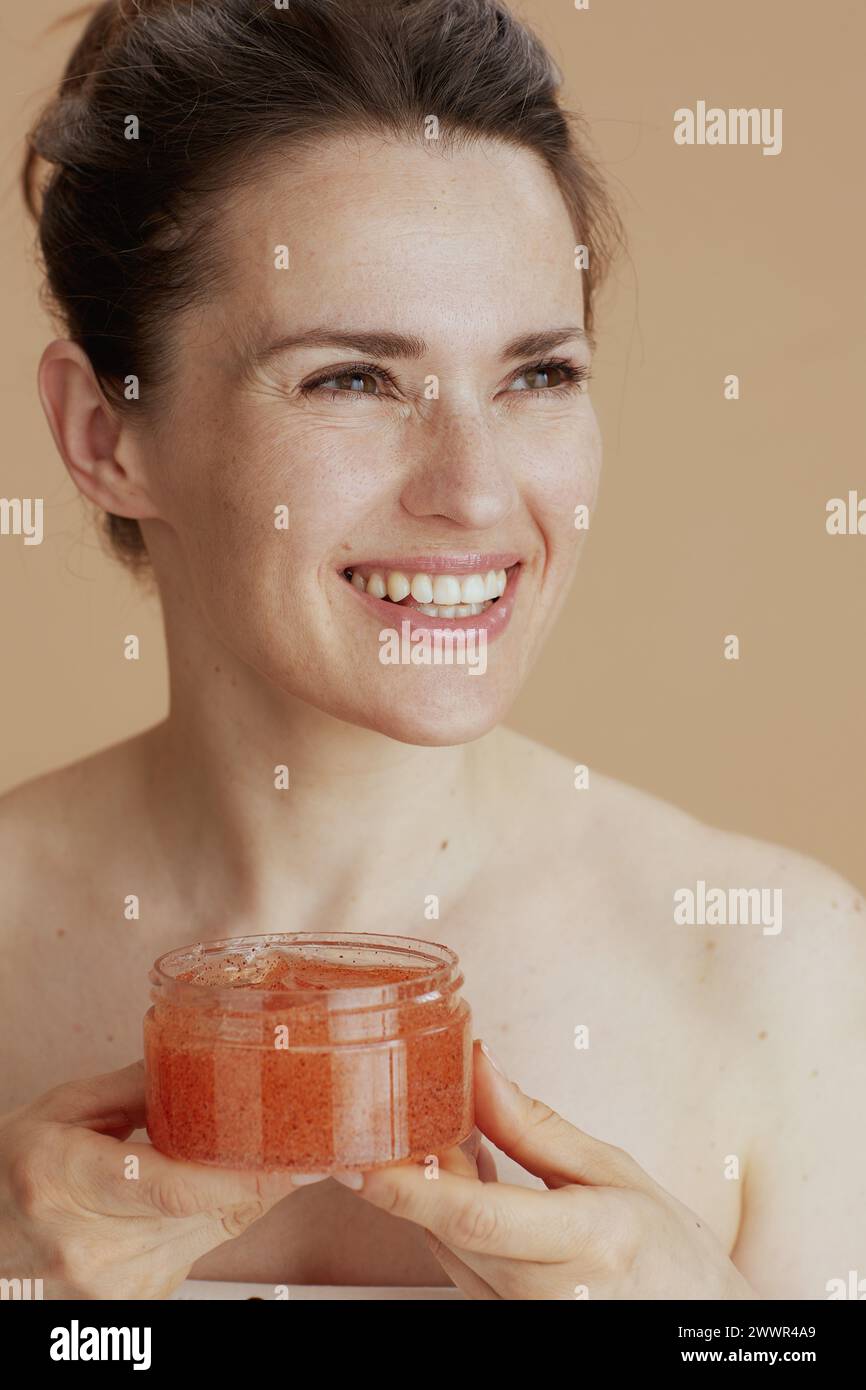happy young woman with face scrub against beige background. Stock Photo