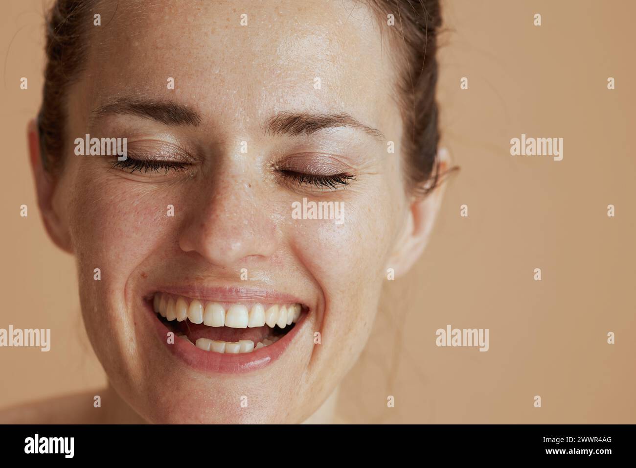 Closeup on happy modern woman with wet face washing isolated on beige