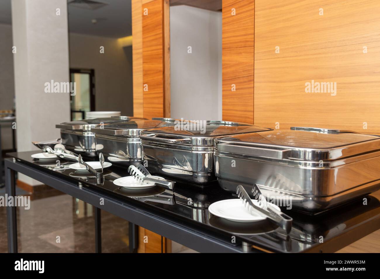 Row of closed chafing dishes at party banquet hall. Marmites ready for service made of stainless steel at buffet. Stock Photo