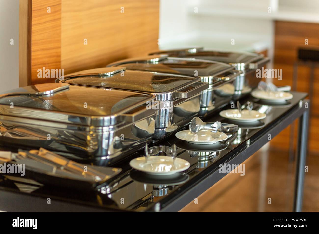 Row of closed chafing dishes at party banquet hall. Marmites ready for service made of stainless steel at buffet. Stock Photo