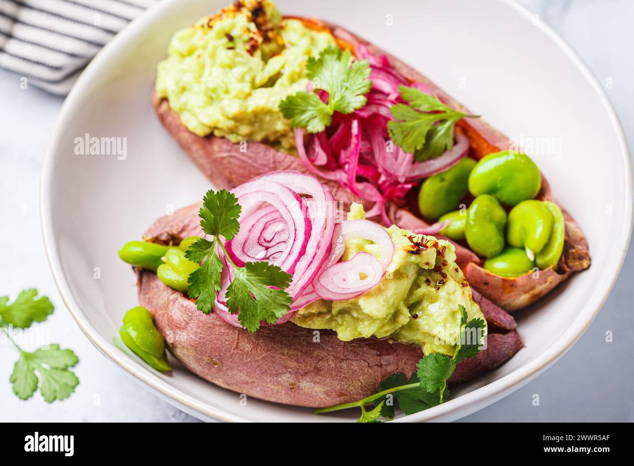 Baked sweet potato halves with guacamole, edamame beans, pickled red onion and cilantro, close-up. Vegan recipe, vegetarian diet food. Stock Photo