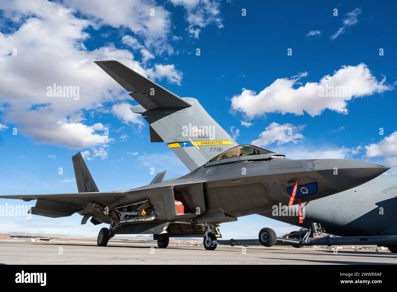 An F-22 Raptor with the 525th Expeditionary Fighter Squadron out of Joint Base Elmendorf-Richardson, Alaska, rests on the airfield after receiving fuel from a C-17 Globemaster III out of Joint Base Charleston, South Carolina, during Exercise Bamboo Eagle 24-1 at Nellis Air Force Base, Nevada, Feb. 2, 2024. Airmen from Yokota Air Base, Japan; Joint Base Pearl Harbor-Hickam, Hawaii; JBER; and JB Charleston, aligned various skillsets to complete the first-ever Air Mobility Command-to-F-22 Raptor refueling. BE 24-1 was a first-of-its-kind exercise directed by the U.S. Air Force Warfare Center and Stock Photo