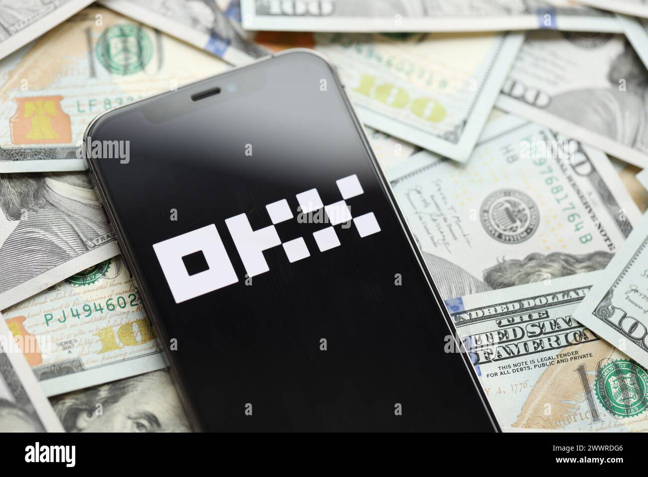 KYIV, UKRAINE - MARCH 15, 2024 OKX logo on iPhone display screen with many hundred dollar bills. Cryptocurrency exchange portal Stock Photo