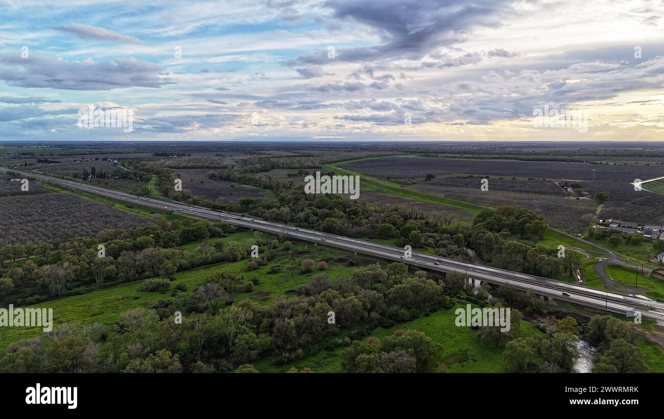An aerial of a road surrounded by green fields and trees Stock Photo