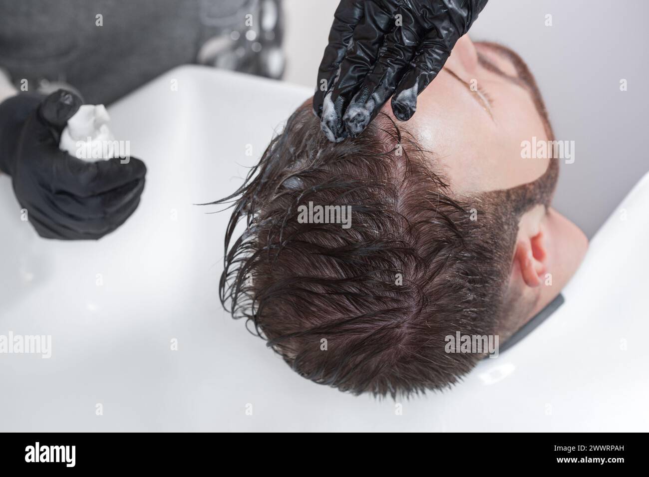 The hairdresser paints hair from gray hair of a man in a barbershop. Stock Photo