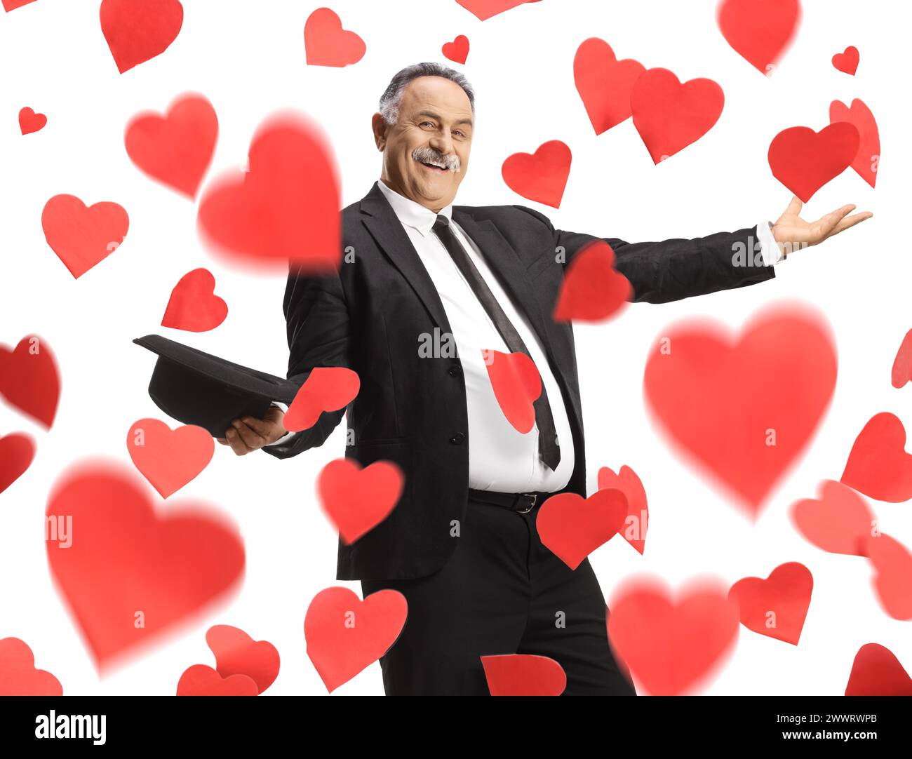 Cheerful mature man in black suit and tie dancing under falling hearts and holding a hat isolated on white background Stock Photo