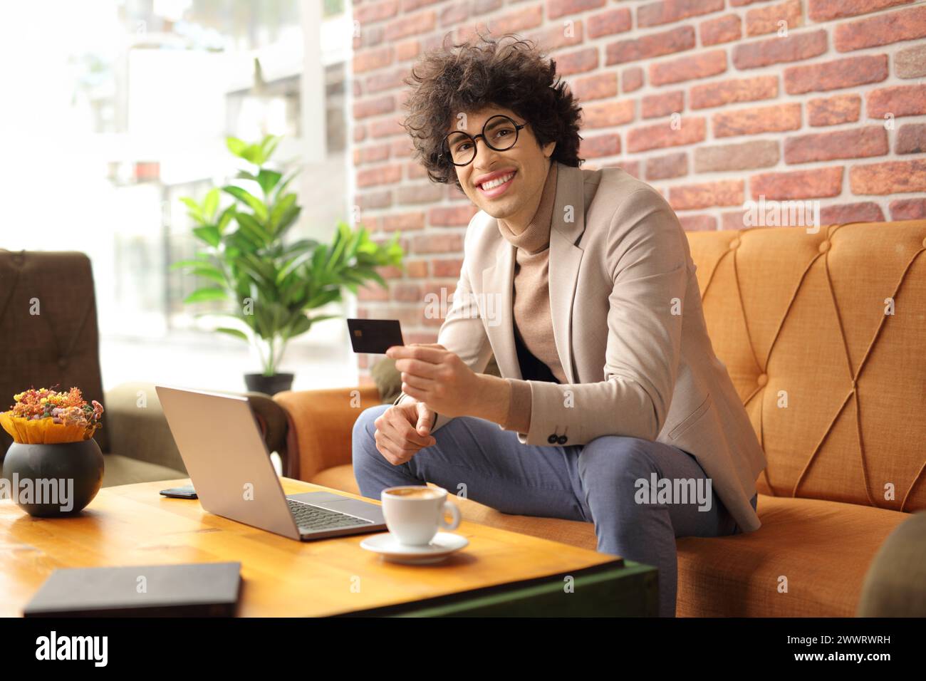 Smiling young man sitting in a cafe using a laptop computer and holding a credit card, online shopping concept Stock Photo