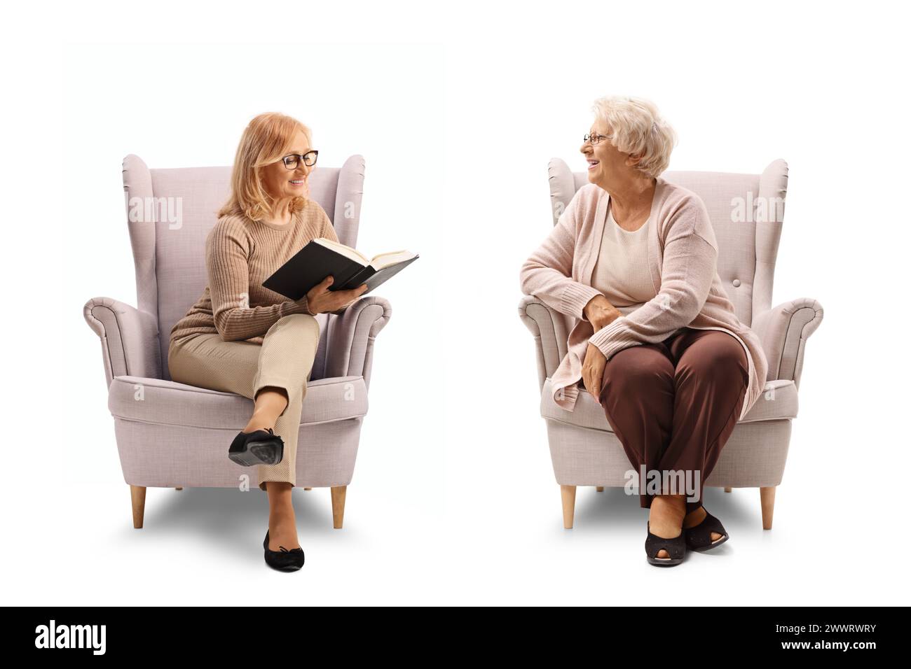 Woman sitting in an armchair and reading a book to an elderly lady ...