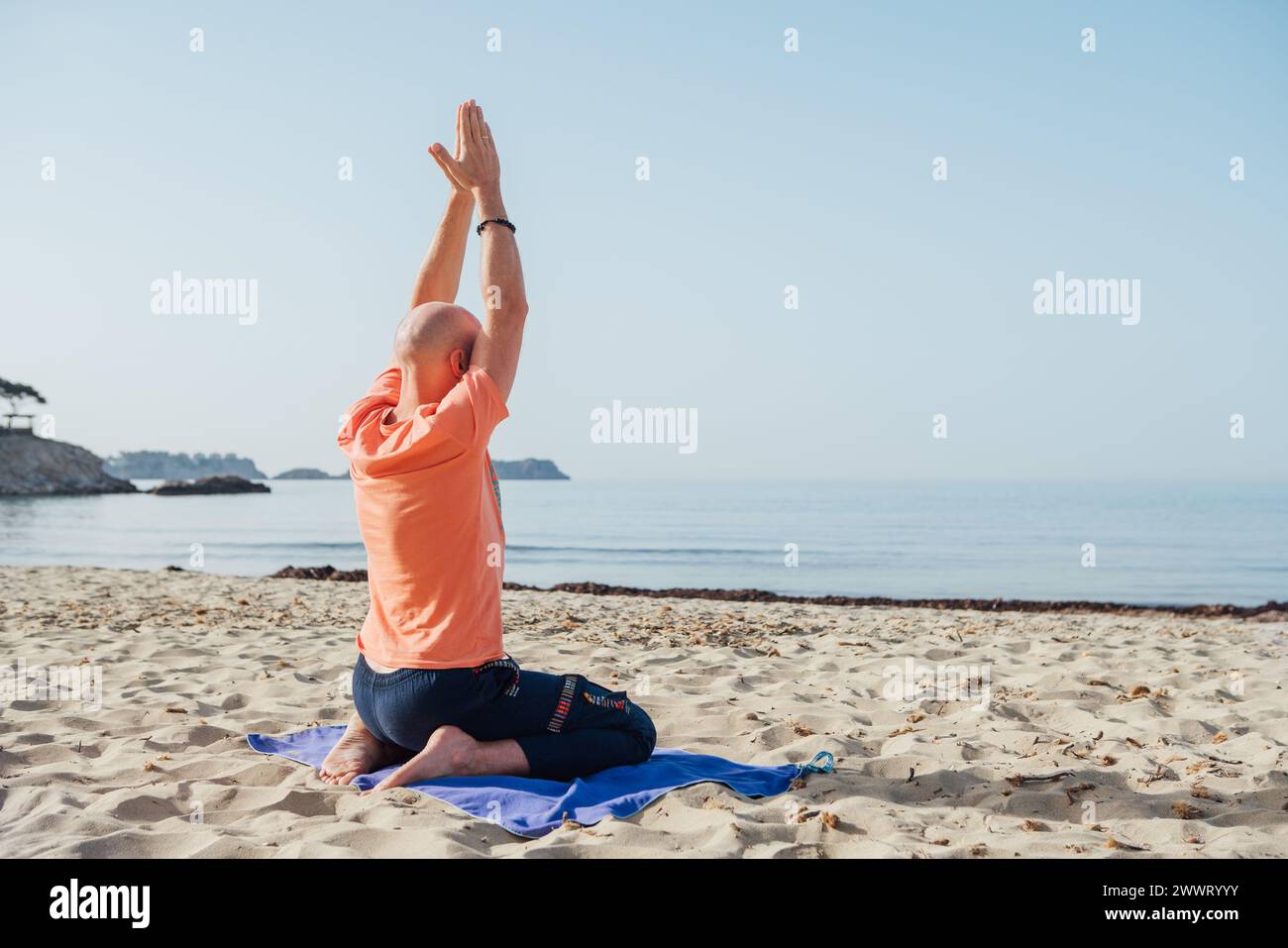 Calm man sitting in Seiza position, doing deep breathing exercises and meditating in early morning hours on the sandy beach with calm sea waves. Menta Stock Photo