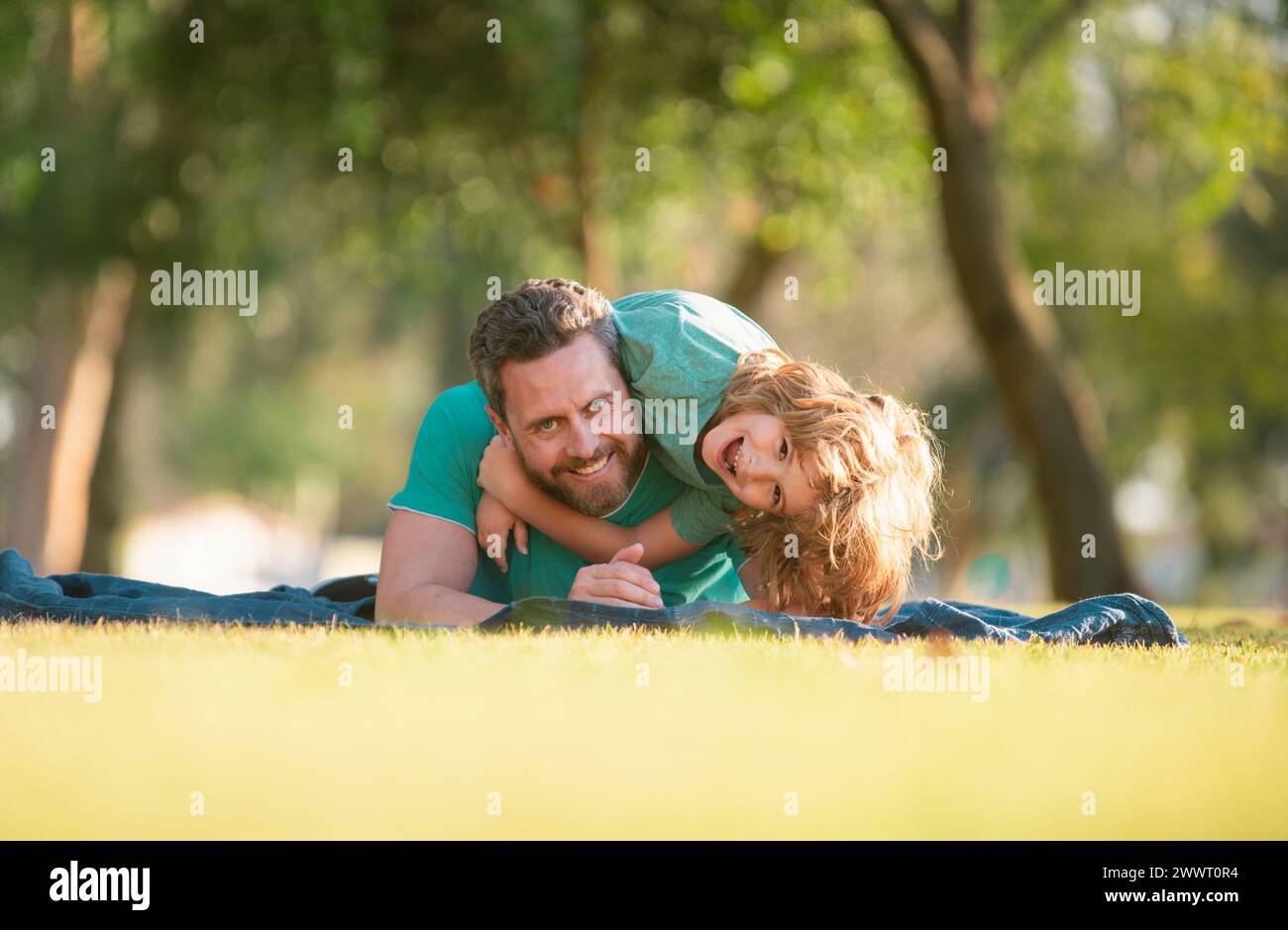 Handsome father piggybacking son playing on nature, daddy holding riding on back adorable cheerful kid boy enjoy active game. Child embracing and Stock Photo