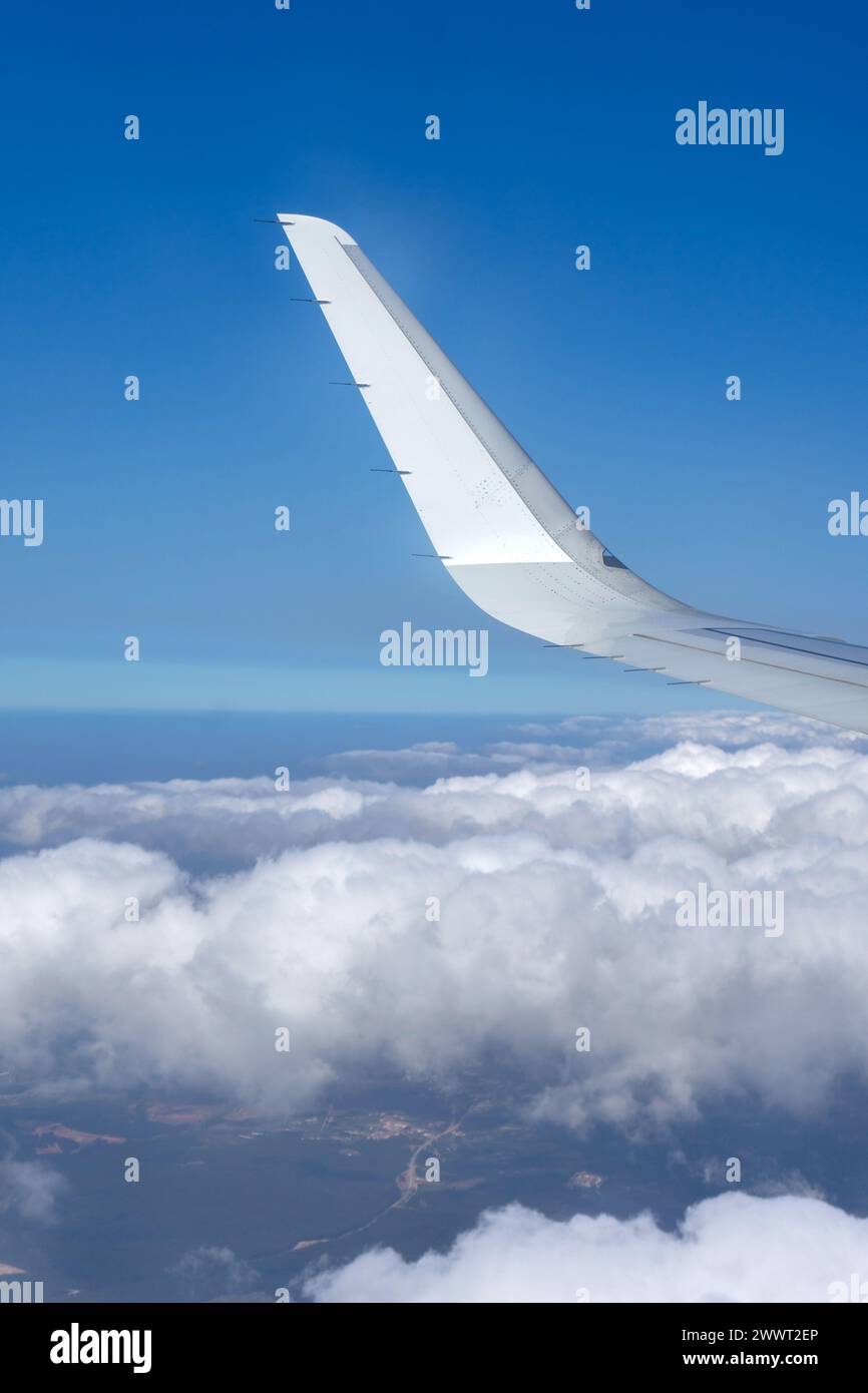 Wing of airplane soaring above fluffy clouds, captured from window seat. Aerial view showcases serene beauty of the sky. Stock Photo