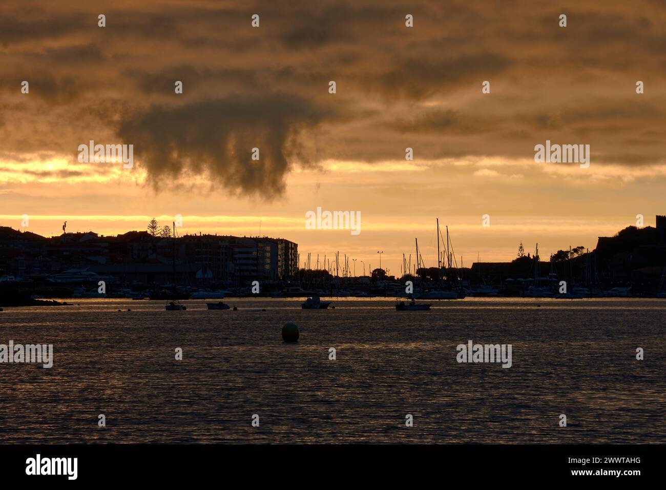 A yellow sunset with a cloud that seems to fall from the sky and in the background the silhouette of the town of Baiona, Pontevedra, Spain Stock Photo