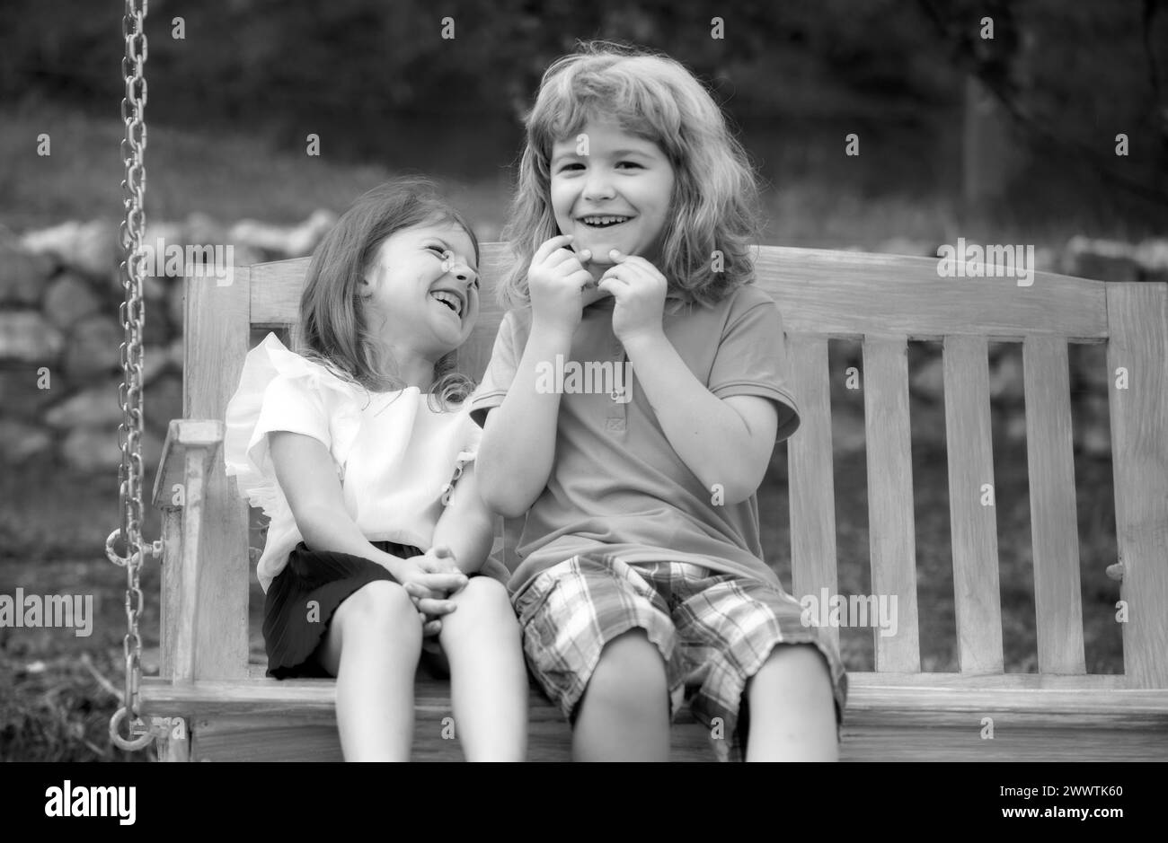 Brother and sister playing outside. Little boy and girl working in the garden. Two happy smiling laughing children swinging on swing in summer park Stock Photo