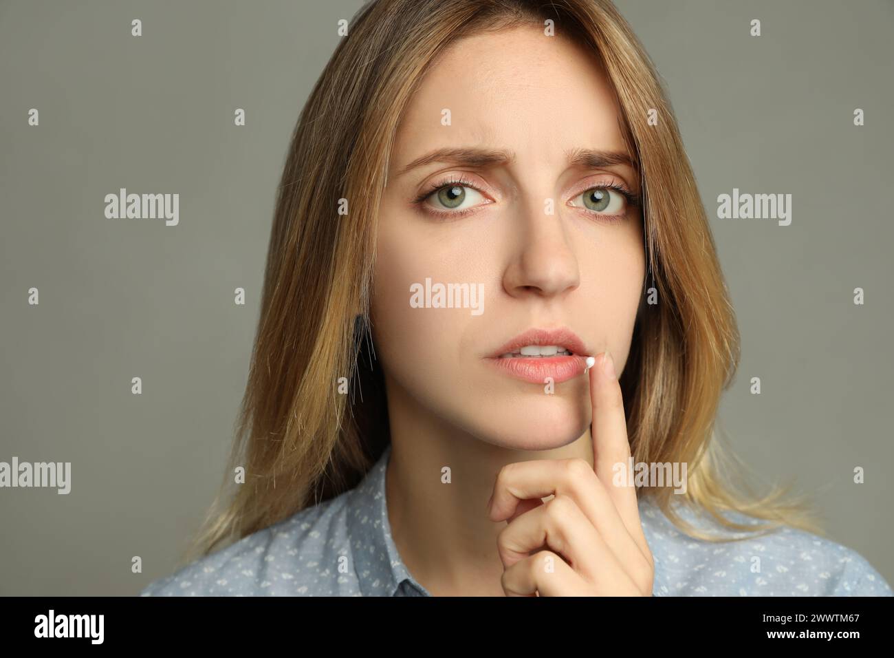 Woman with herpes applying cream onto lip against  light grey background Stock Photo