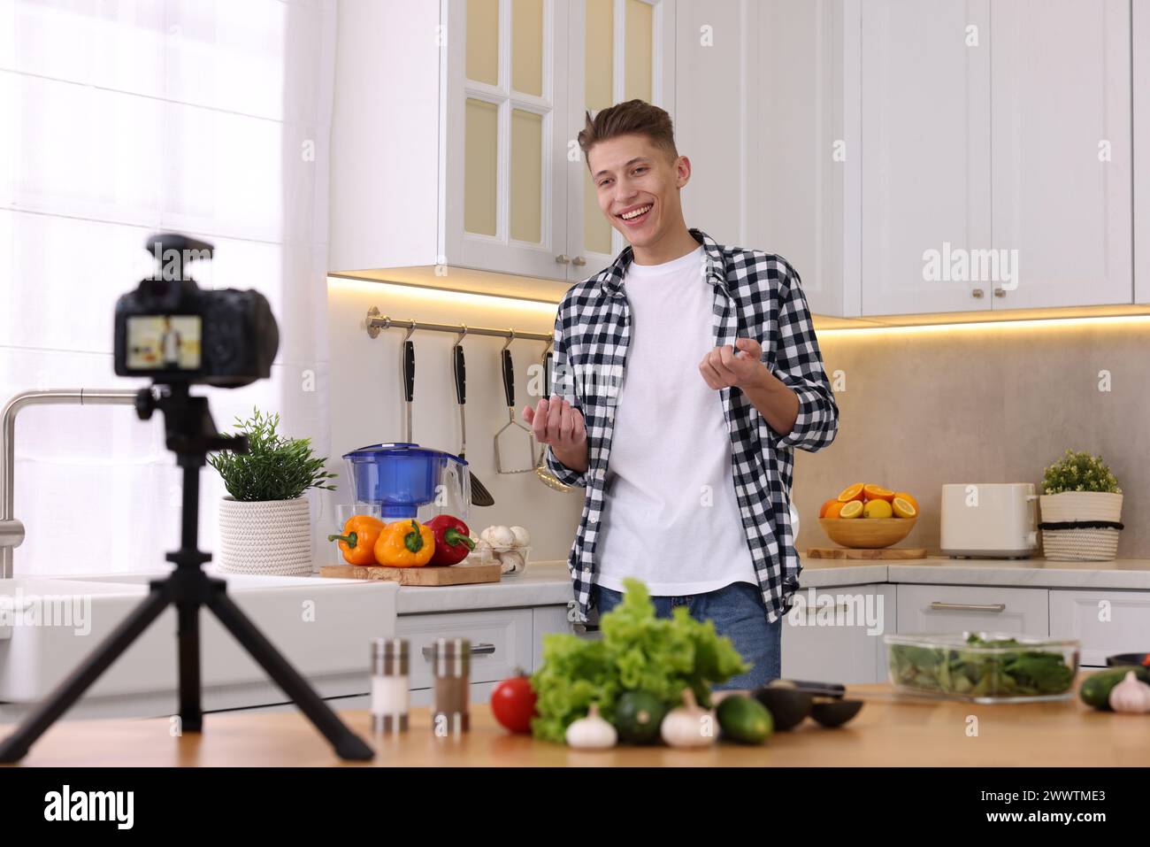 Smiling food blogger explaining something while recording video in kitchen Stock Photo