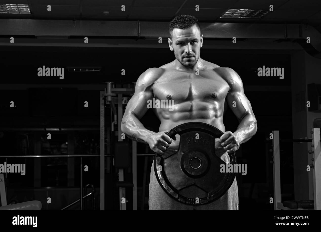 Powerlifter with weight disk in sport gym. Bodybuilder with heavy disk