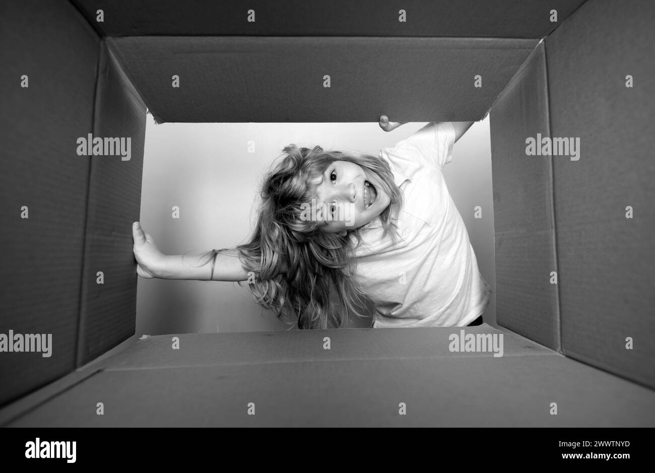 Kid unpacking and opening carton box, and looking inside with surprise face. Open big box. Stock Photo