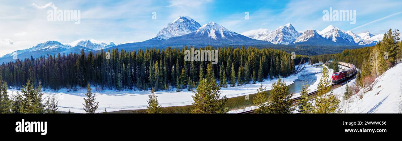 Panorama of Morant's Curve in Banff National Park with Mount Temple overlooking as red cargo train passes through. Beautiful snowy winter landscape in Stock Photo