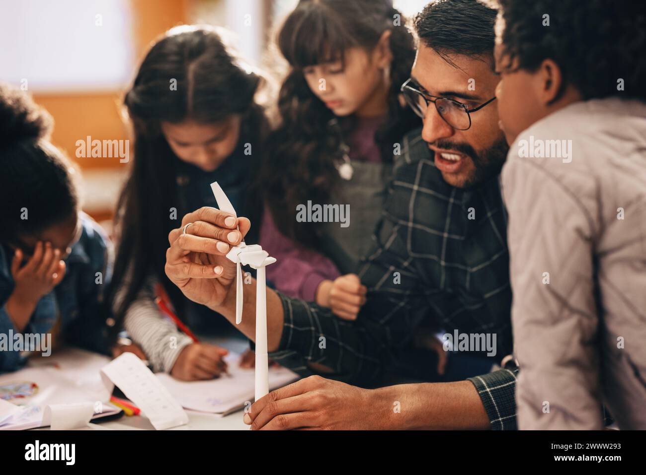 Children learning about renewable energy with a 3D windmill model in science class. Male elementary school teacher giving a practical lesson on wind p Stock Photo