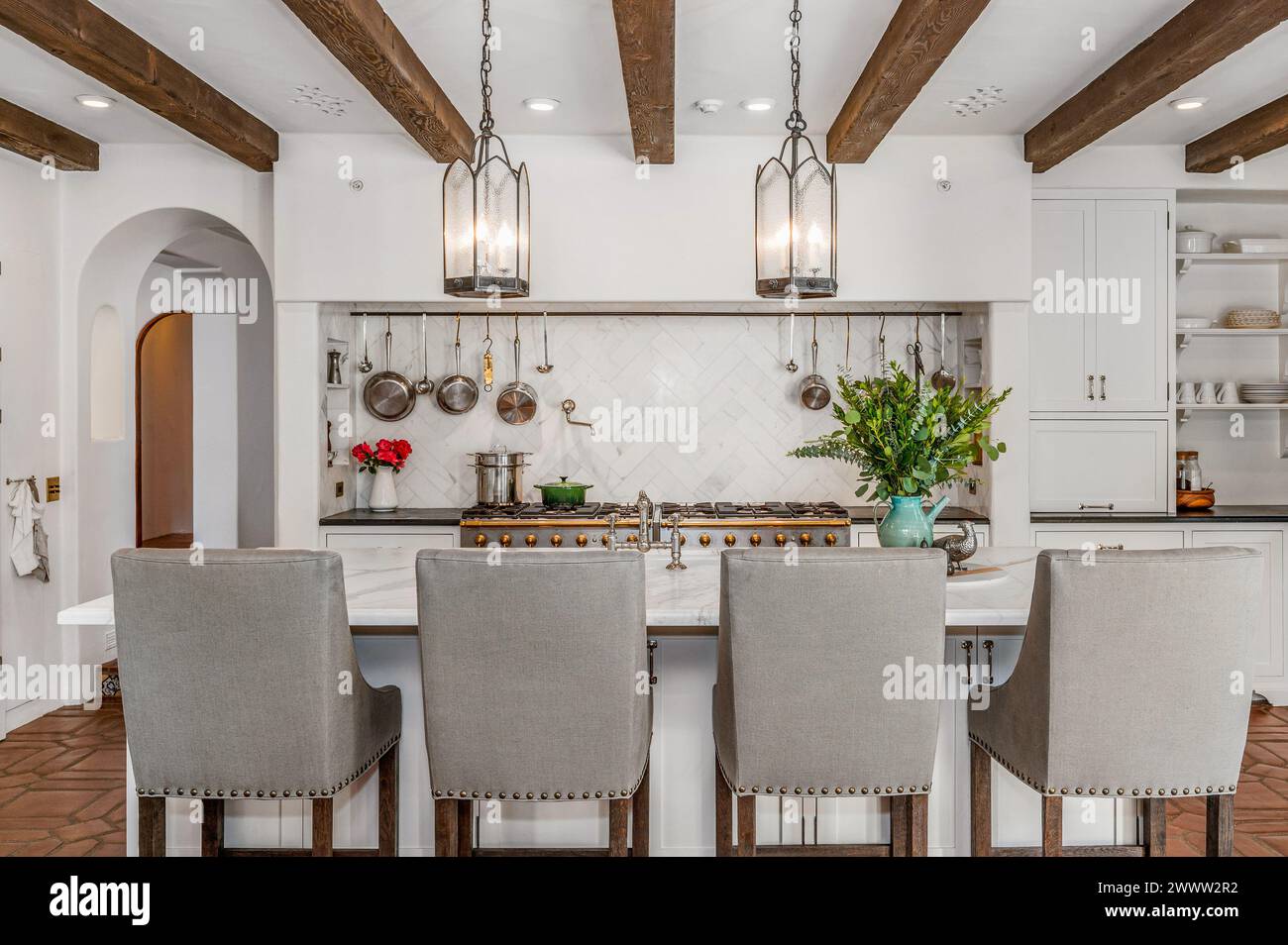 A modern kitchen with white walls, wooden beams, counters, and chairs Stock Photo