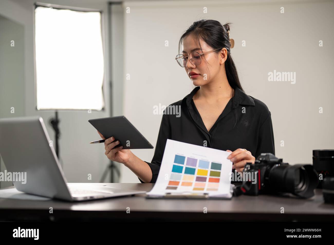 A professional, focused Asian female photographer is looking at a color checker, checking color, working in a photoshoot studio. Stock Photo