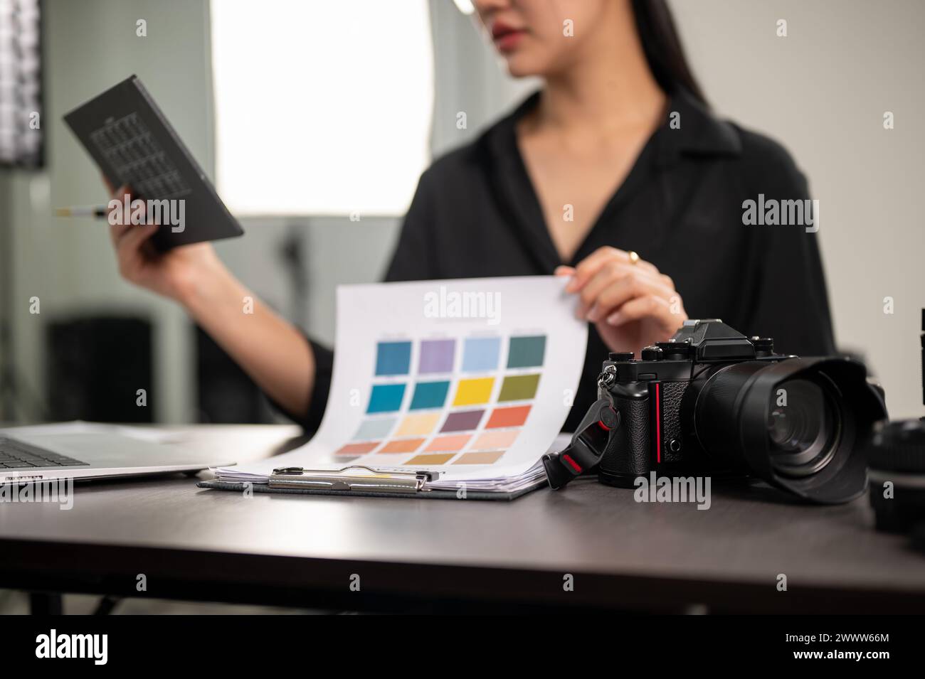 A close-up image of a professional DSLR camera on a desk in a studio, a female photographer is checking color on a color checker. selective focus Stock Photo