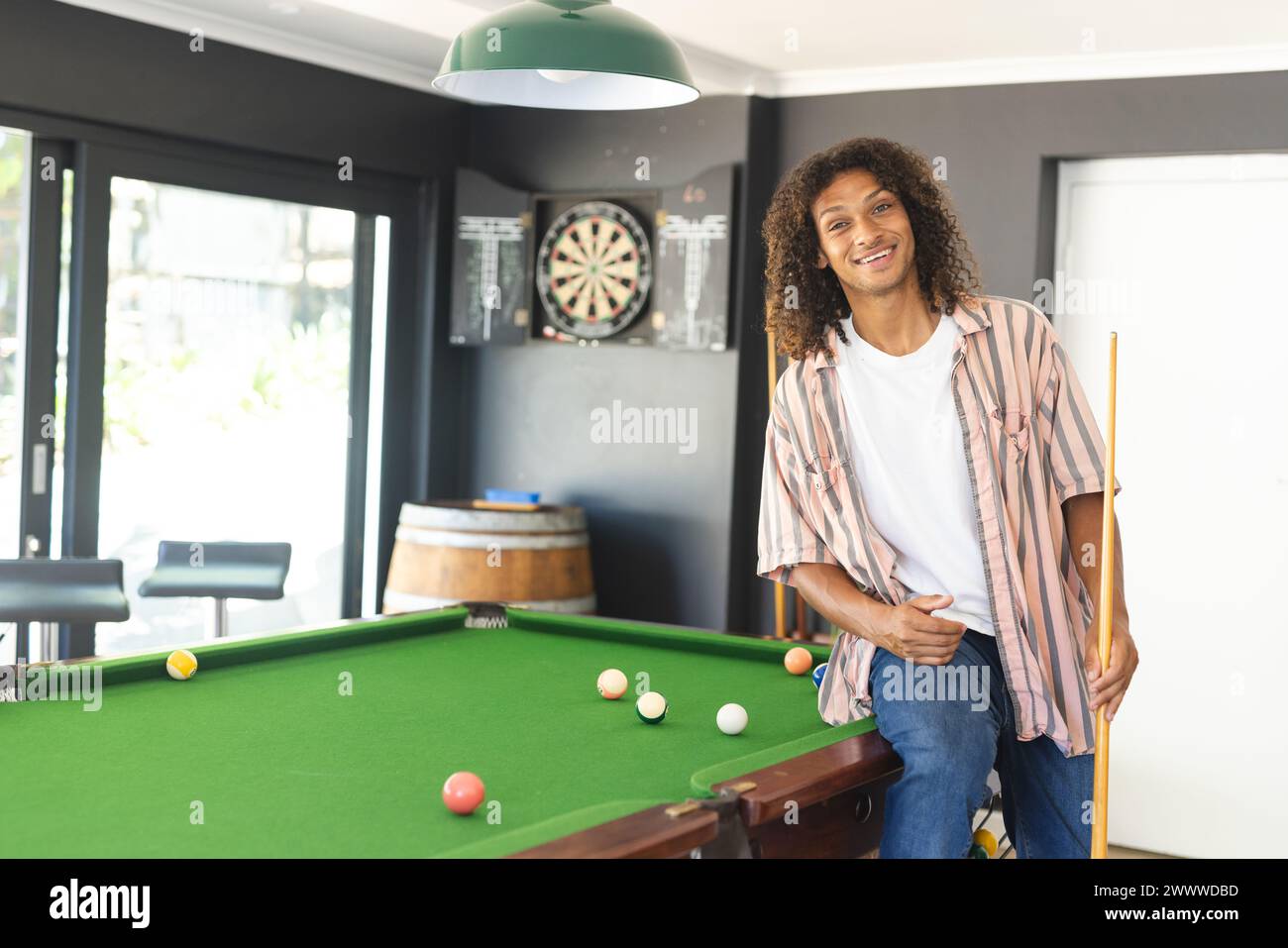 A young African American man with curly hair stands by a pool table with copy space Stock Photo