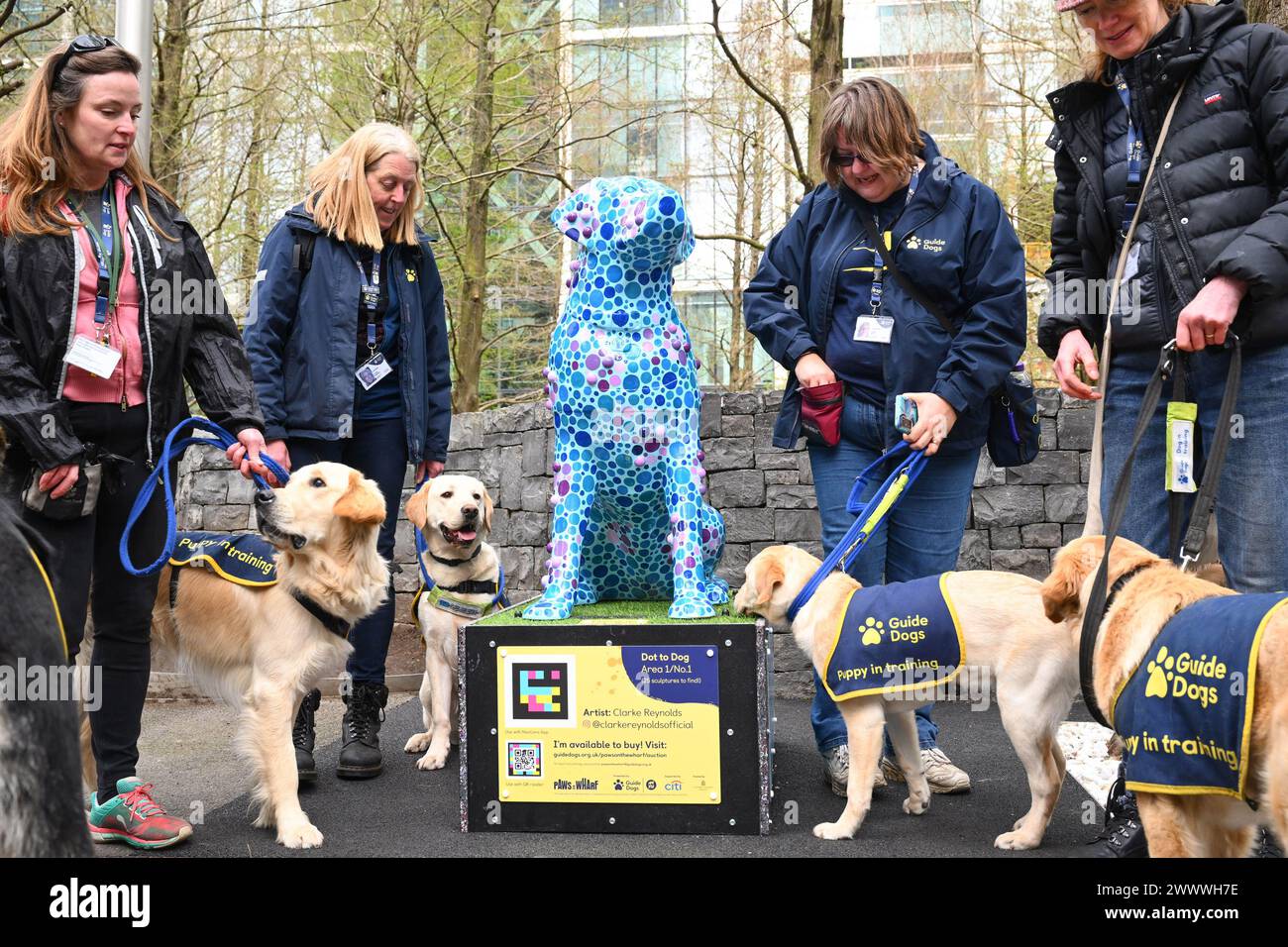 EDITORIAL USE ONLY Volunteer Puppy Raisers (l-r) Louise Roche, Annie Hawkins, Sally Ross, and Annette Fettes and guide dog puppies, with one of 25 artist-designed dog sculptures that make up 'Paws on the Wharf ', a sculpture trail created by Guide Dogs in partnership with Wild in Art and hosted by Canary Wharf Group (CWG). Issue date: Tuesday March 26, 2024. Stock Photo