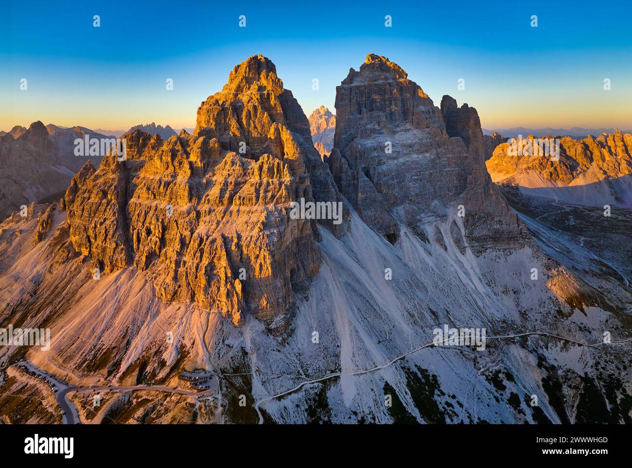 Aerial view from high altitude of Tre Cime di Lavaredo peaks orange lit by the setting sun, with a Dolomites mountain panorama. Stock Photo